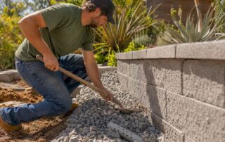 Hands placing angular stone behind retaining wall